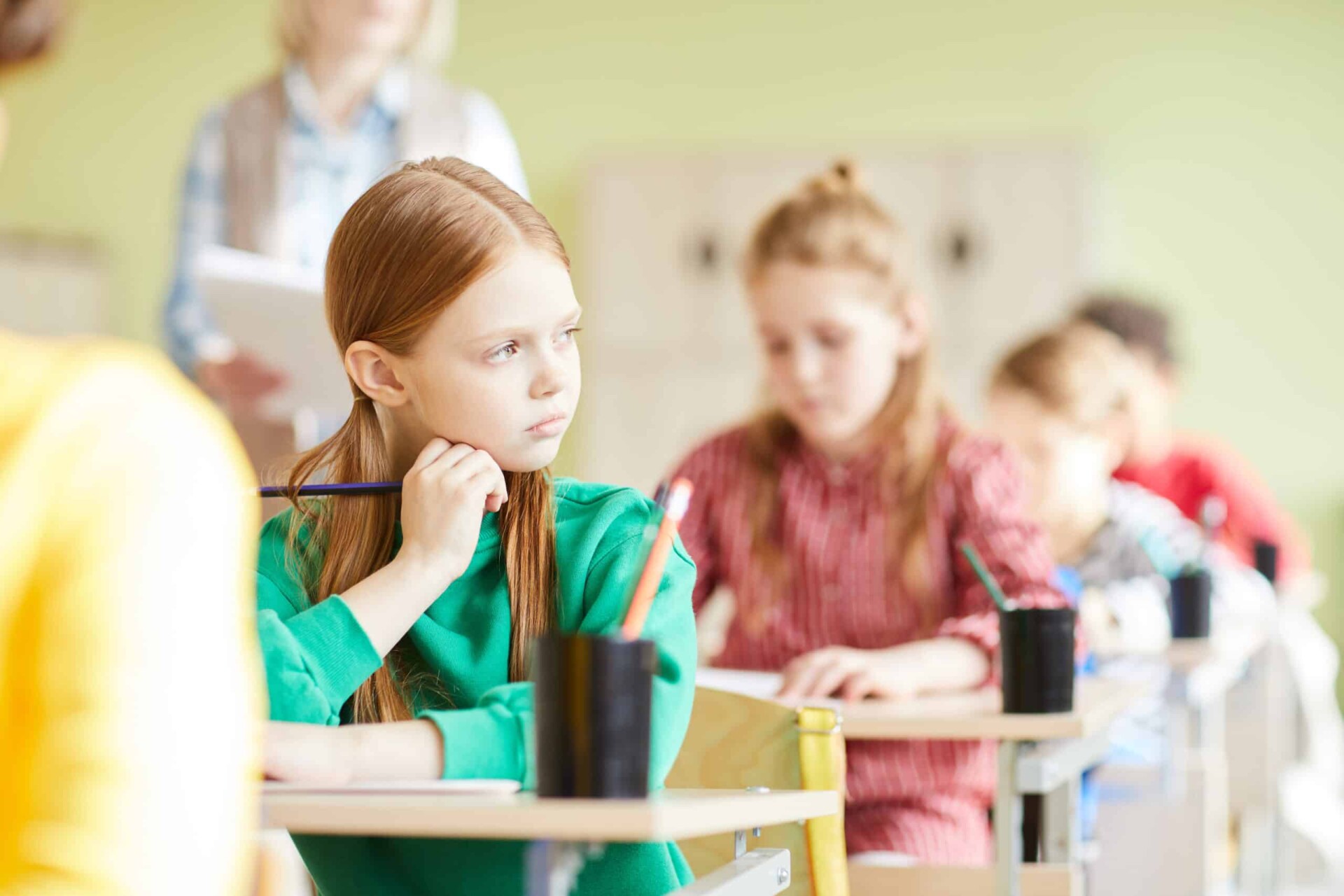 Aluna triste e pensativa com rabo de cavalo e lápis sentado na mesa e olhando de lado na sala de aula